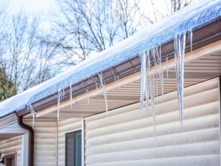 A large ice dam with hanging icicles on a home with off-white siding